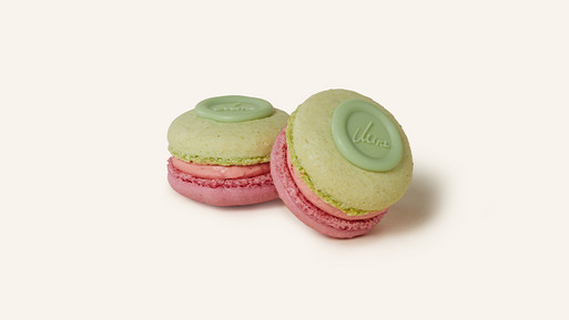 Zwei Erdbeer-Limette-Basilikum-Macarons mit einer zartgrünen Schale und einer fruchtig-frischen rosa Füllung. Verziert mit einem grünen Mira-Schokosiegel, das aus der Kooperation mit der Fernsehköchin Mira Maurer stammt, vereinen sie kreative Aromen mit meisterhafter Eleganz – ein außergewöhnlicher Genuss aus der Breuninger Confiserie.