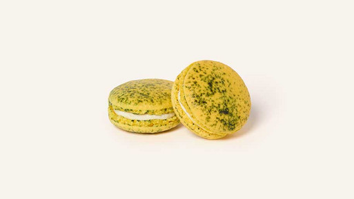 Zwei gelbe Limoncello-Macarons mit leicht gesprenkelter Oberfläche und heller Cremefüllung auf hellem Hintergrund.