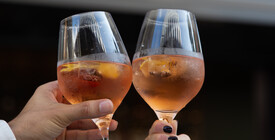 Zwei Aperitifgläser mit einem fruchtigen Getränk werden angestoßen.