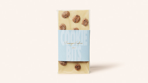 Weiße Schokoladentafel mit Keksstücken und Papierbanderole auf hellem Hintergrund.