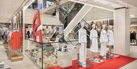 Breuninger-Verkaufsfläche mit rotem „B“-Element, Treppe im Hintergrund und Schaufensterpuppen in weißer Designermode auf rotem Teppich.