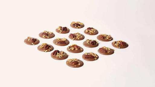 Viele kleine, runde Schokoladentaler (Palets au Chocolat) mit Topping in Rasteranordnung auf hellem Hintergrund – feine, französische Schokoladenplätzchen mit raffiniertem Finish aus der Breuninger Confiserie.