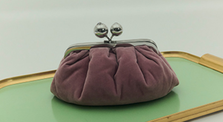 Eine braune Tasche mit silbernem Verschluss wird auf einem grünen Tablett mit goldenem Rand präsentiert.