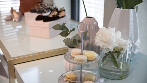 Dekorativer Tisch mit Macarons auf einer Etagere, Blumenvasen und Schuhen im Hintergrund.