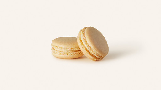 Zwei helle Macarons mit Cremefüllung auf hellem Hintergrund.