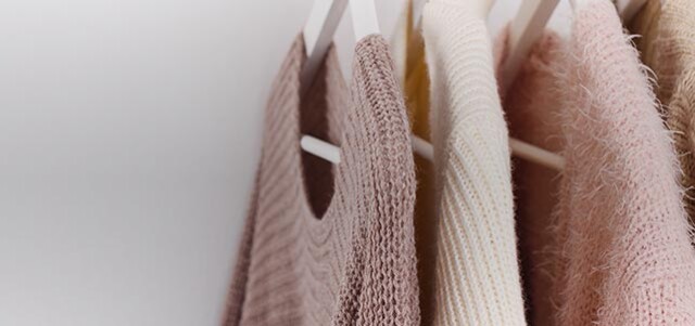 Mehrere farblich sortierte Strickpullover hängen ordentlich auf Kleiderbügeln in einer Reihe