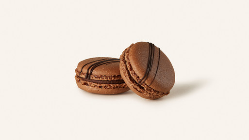 Zwei braune Macarons mit Cremefüllung auf hellem Hintergrund.