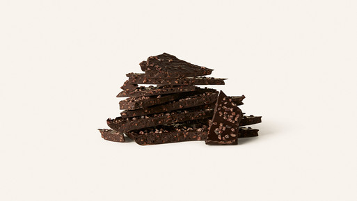 Gestapelte Bruchstücke dunkler Schokolade mit Nussanteilen auf hellem Hintergrund.