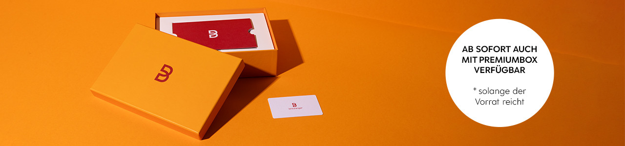 Orange Box mit Breuninger-Logo, rote und weiße Karte, Text: „Ab sofort auch mit Premiumbox verfügbar“.