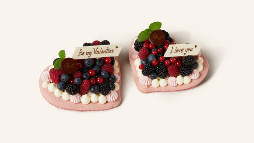 Zwei herzförmige Törtchen mit Beeren und dekorativen Schokoladentäfelchen mit Liebesbotschaften.