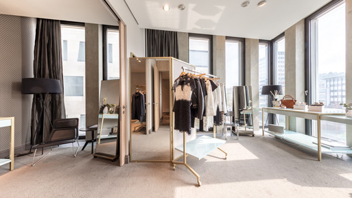 Moderner Showroom mit Kleiderständern, Spiegeln, Präsentationstischen und großen Fenstern mit Tageslicht.
