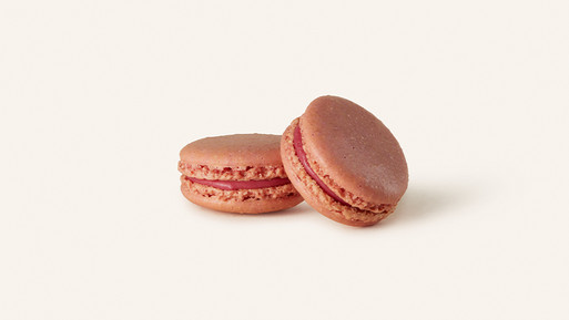 Zwei rosafarbene Macarons mit Cremefüllung auf hellem Hintergrund.