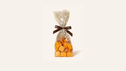 Beutel mit Tartufo in orangenem Papier eingeschlagen, verpackt in transparenter Folie mit Schleife auf hellem Hintergrund.