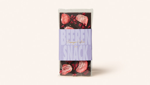 Schokoladentafel mit gefriergetrockneten Beeren und Papierbanderole auf hellem Hintergrund.