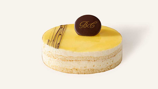 Edle Grand Manier Torte mit hellem Biskuitboden und feiner Schokolade-Filigran-Dekoration auf der cremigen Oberfläche, gekrönt mit einem BC-Schokoladensiegel der Breuninger Confiserie – ein luxuriös-cremiger Genussmoment.