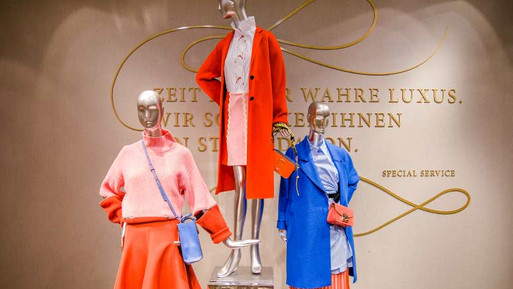 Drei Schaufensterpuppen mit farbigen Damenoutfits vor einer Wand mit goldener Schrift in einem eleganten Innenraum.