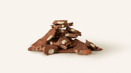 Gestapelte Bruchstücke Milchschokolade mit ganzen Mandeln auf hellem Hintergrund.