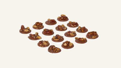 Viele kleine, runde Palets au Chocolat aus Nuss-Vollmilch-Schokolade mit feinem Nuss-Topping in Rasteranordnung auf hellem Hintergrund – feine, französische Schokoladenplätzchen mit nussig-cremem Finish aus der Breuninger Confiserie