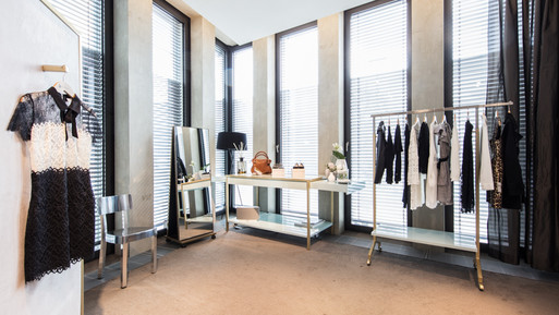 Heller Showroom mit Kleiderständern, Präsentationstisch, Spiegeln und bodentiefen Fenstern mit Jalousien.