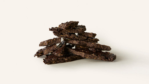 Gestapelte Bruchstücke dunkler Schokolade mit Frucht- und Nussanteilen auf hellem Hintergrund.