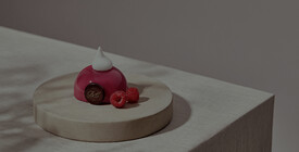 Elegantes Dessert in glänzendem Rot mit Himbeeren, garniert auf einer runden Platte.