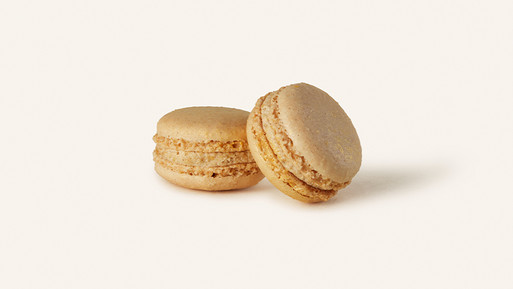 Zwei hellbeige Macarons mit Cremefüllung auf hellem Hintergrund.