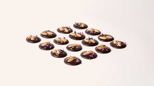Viele kleine, runde Palets au Chocolat aus Zartbitter-Schokolade mit feinem Topping in Rasteranordnung auf hellem Hintergrund – feine, französische Schokoladenplätzchen mit intensivem Zartbitter-Finish aus der Breuninger Confiserie.