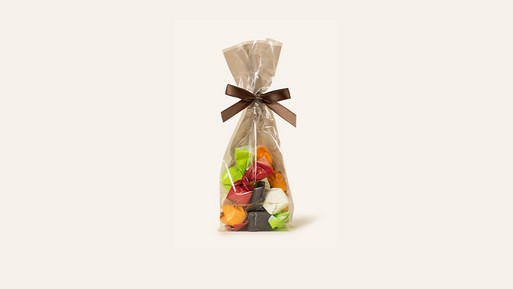 Beutel mit Tartufo in buntem Papier eingeschlagen, verpackt in transparenter Folie mit Schleife auf hellem Hintergrund.