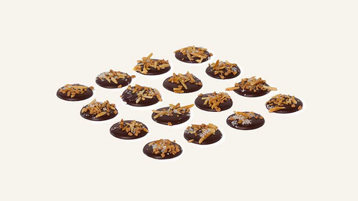 Viele kleine, runde Palets au Chocolat aus Vollmilch-Schokolade mit feinem Topping in Rasteranordnung auf hellem Hintergrund – feine, französische Schokoladenplätzchen mit cremig-süßem Vollmilch-Finish aus der Breuninger Confiserie.