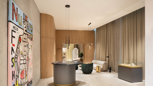 Moderner Beratungsraum mit runden Sitzpodesten und einem zentralen Tisch. Helle Holzvertäfelung, bodentiefe Vorhänge und dezente Deckenbeleuchtung schaffen eine ruhige, hochwertige Atmosphäre. An der linken Wand hängt ein farbenfrohes Kunstwerk, im Hintergrund stehen gepolsterte Sessel und ein freistehender Spiegel.