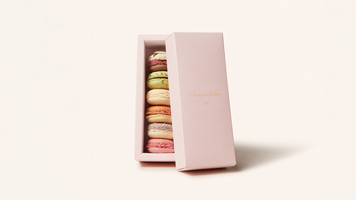 Eine elegante, rosafarbene Macaron Geschenkbox, leicht geöffnet, die eine Auswahl feinster Macarons aus der Breuninger Confiserie offenbart. Die Macarons sind sorgfältig arrangiert und bestechen durch ihre vielfältigen Farben, die pure Genussmomente versprechen. Ein perfektes Geschenk voller Raffinesse und Qualität.