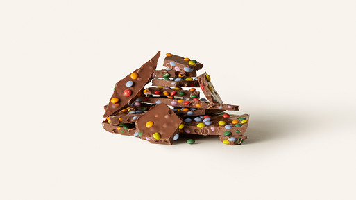 Gestapelte Bruchstücke Milchschokolade mit bunten Zuckerdragées auf hellem Hintergrund.