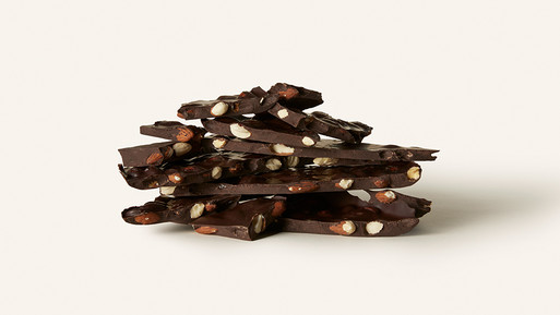 Gestapelte Bruchstücke dunkler Schokolade mit ganzen Mandeln auf hellem Hintergrund.