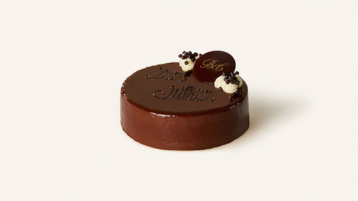 Runde Schokoladentorte mit glänzender Glasur, dekoriert mit Schokoladenelementen und der Aufschrift „Alles Liebe zum Jubiläum“.