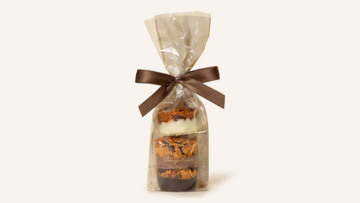 Ein elegantes Arrangement aus feinen Florentiner Krönchen aus der Breuninger Confiserie, liebevoll verpackt in einer transparenten Cellophantüte, die den Blick auf die köstlichen Details freigibt. Die Florentiner haben verschieden Schokoladenböden – darunter weiße, Vollmilch- und Zartbitterschokolade. Die Verpackung wird durch eine hochwertige, dunkelbraune Schleife gekrönt, die das Gesamtbild zu einem perfekten Geschenkabrundet. Ein Genuss für alle Sinne, der die traditionsreiche Handwerkskunst der Breuninger Confiserie widerspiegelt und sich ideal für besondere Anlässe