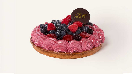 Sommerbeeren-Traum-Tarte mit knusprigem Mürbeteigboden, gefüllt mit zartem rosafarbenem Beerencreme und reichlich belegt mit frischen, glänzend glasierten Sommerbeeren wie Himbeeren, Erdbeeren und Brombeeren, gekrönt mit einem BC-Schokoladensiegel der Breuninger Confiserie – ein verführerisch-fruchtiger Sommergenussmoment.