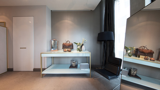 Moderner Showroom mit Präsentationstisch, Spiegel, Sitzmöbel und dekorativen Accessoires vor gemusterter Wand.