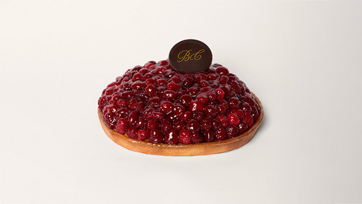 Verführerische Himbeertarte auf knusprigem Mürbeteigboden, deren Oberseite vollständig mit glänzenden, saftigen Himbeeren bedeckt ist, gekrönt mit einem dunklen Schokoladensiegel mit goldenem „BC"-Logo – ein erlesener Genuss aus der Breuninger Confiserie