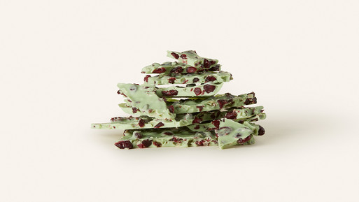 Gestapelte Bruchstücke grüner Schokolade mit Fruchtstücken auf hellem Hintergrund.