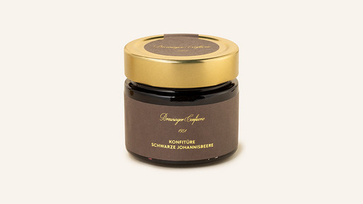 Glas mit Schwarzer-Johannisbeer-Konfitüre und goldenem Schraubdeckel auf hellem Hintergrund.