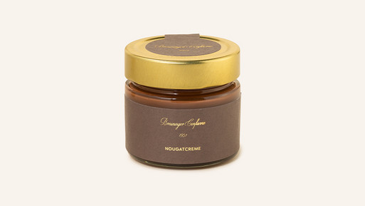 Glas mit Nougatcreme und goldenem Schraubdeckel auf hellem Hintergrund.