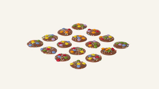 Viele kleine, runde Palets au Chocolat aus Vollmilch Schokolade mit bunten Schokolinsen in Rasteranordnung auf hellem Hintergrund – feine, französische Schokoladenplätzchen mit farbenfrohem, spielerischem Finish aus der Breuninger Confiserie.
